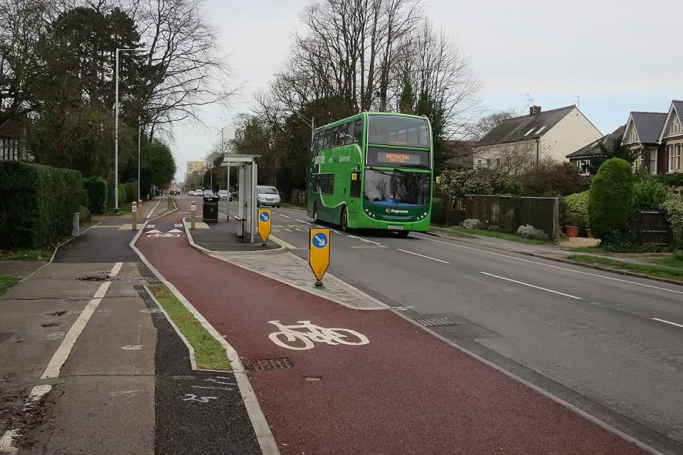 Red painted bike lane next to floating bus stop and green double-decker bus in the UK.